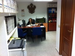 Foto de uno de nuestros despachos. Se puede ver un despacho amplio con estanterías y una mujer sentada en frente de una mesa de oficina.